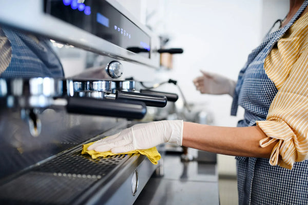 Barista performing maintenance on a professional coffee machine with a descaler in a commercial kitchen