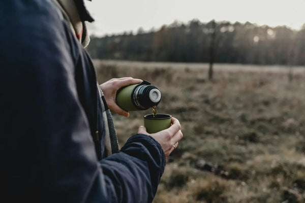 hiker pouring outdoor coffee from a thermos at the top of a trail at sunrise