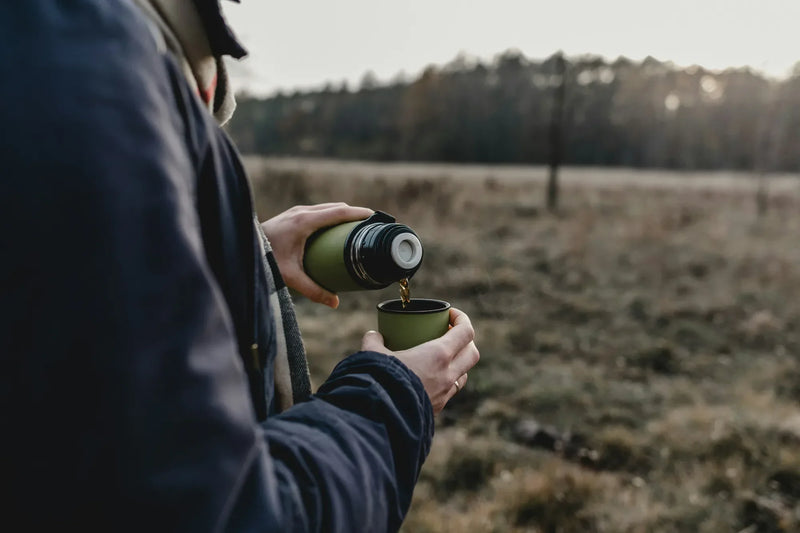 hiker pouring outdoor coffee from a thermos at the top of a trail at sunrise