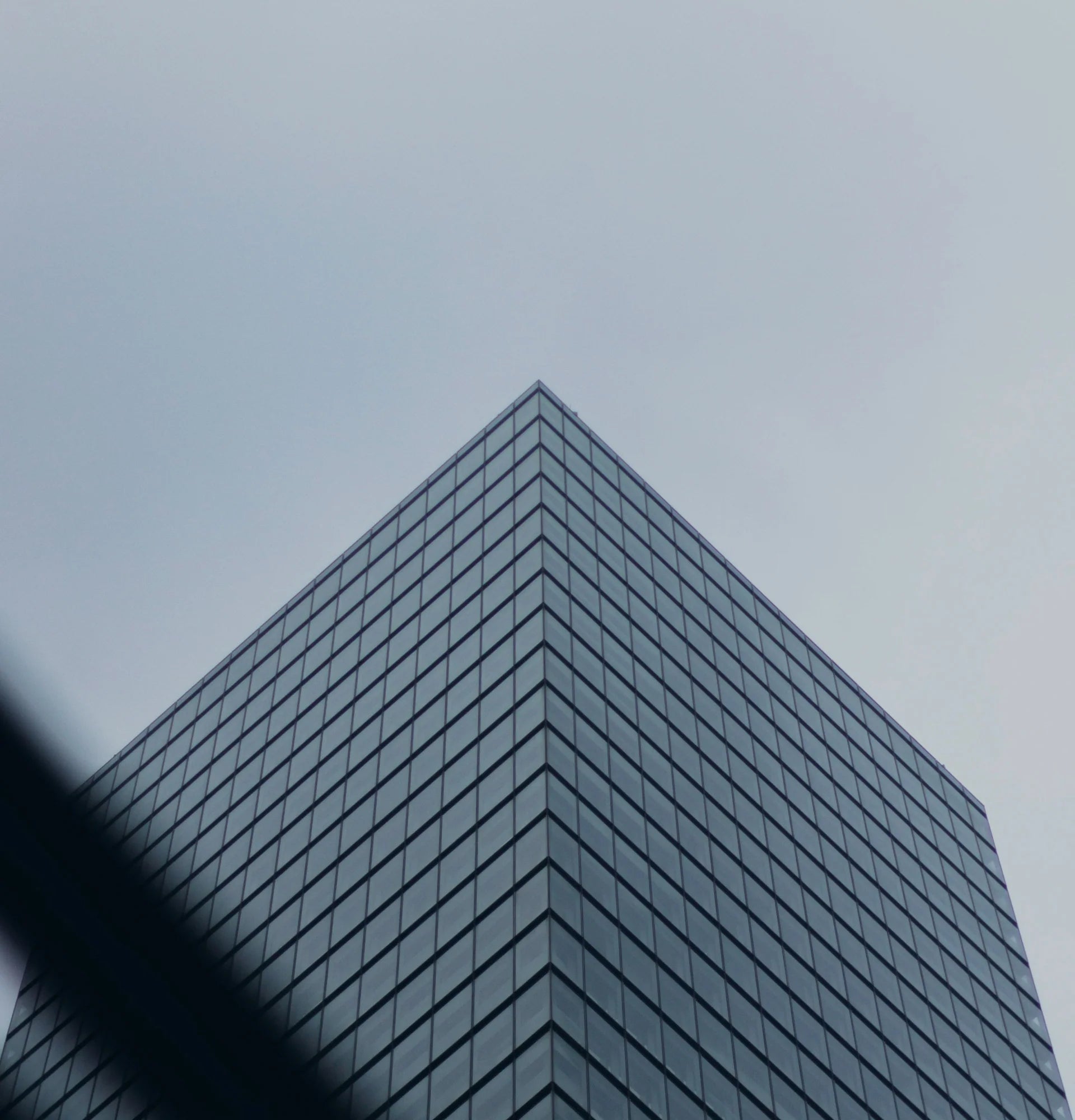 Corner view of a modern glass office tower rising into an overcast sky.